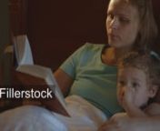 Tilt shot of mother and son in bed at night. Mom reading aloud before bed, boy watching TV - License this clip: https://fillerstock.com/video/1822